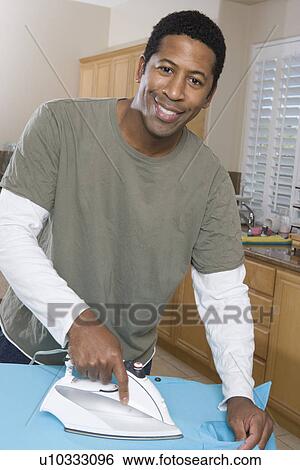 Stock Photograph - Mid-adult man ironing shirt in domestic kitchen. Fotosearch