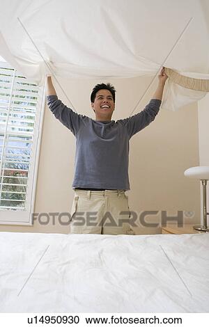 Stock Image - Mid-adult man making a bed. Fotosearch