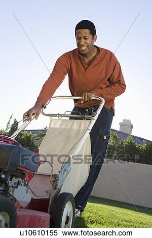 Stock Photography - Mid-adult man mowing lawn, smiling. Fotosearch