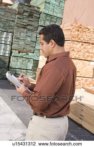 Stock Image - Mid-adult man stock-taking in warehouse. Fotosearch