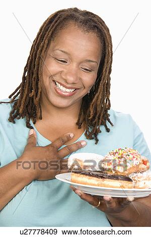 Stock Photo - Mid-adult overweight woman holding plate with donuts and smiling. Fotosearch