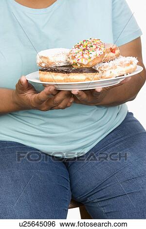 Stock Photograph - Mid-adult overweight woman holding plate with donuts.. Fotosearch