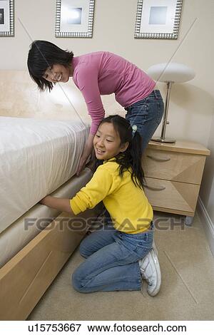 Stock Photo - Mid-adult woman and her daughter making a bed. Fotosearch