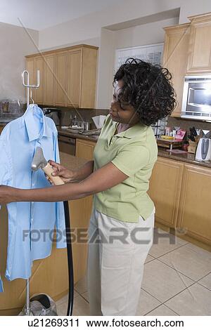Stock Image - Mid-adult woman cleaning shirt in domestic kitchen. Fotosearch