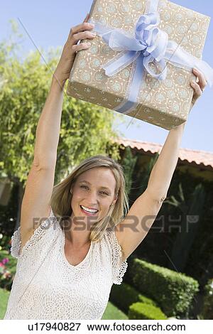 Stock Photo - Mid-adult woman holding aloft her birthday present, smiling. Fotosearch
