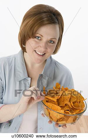 Stock Image - Mid-adult woman holding bowl of potato chips. Fotosearch
