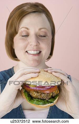 Stock Image - Mid-adult woman holding hamburger. Fotosearch