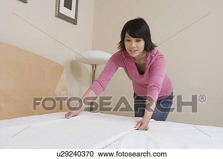Stock Image - Mid-adult woman making a bed. Fotosearch