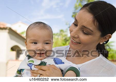 Stock Image - Mother holding baby (6-12 months), outdoors. Fotosearch