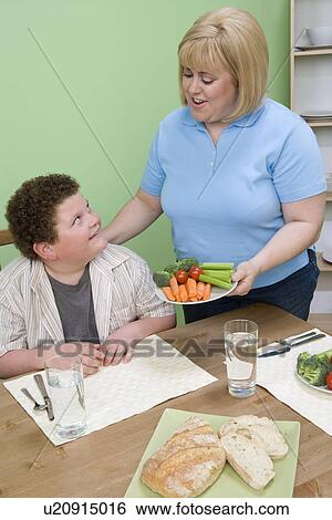 Stock Photograph - Mother serving her overweight son healthy meal. Fotosearch