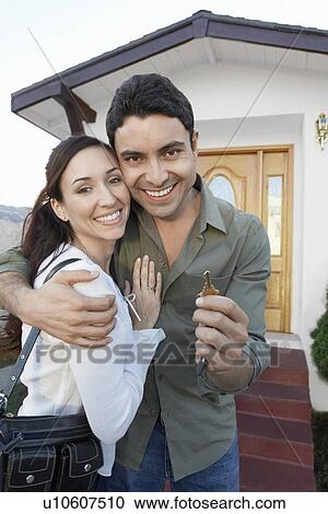 Stock Image - New homeowners standing in front of house holding key, portrait. Fotosearch