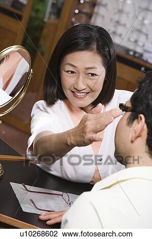 Stock Image - Optician with customer in store. Fotosearch
