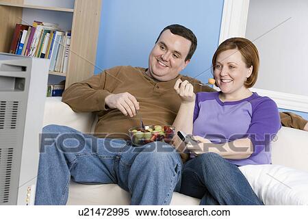 Overweight couple eating fruit on sofa View Large Photo Image Stock Photography - Overweight couple eating fruit on sofa. Fotosearch