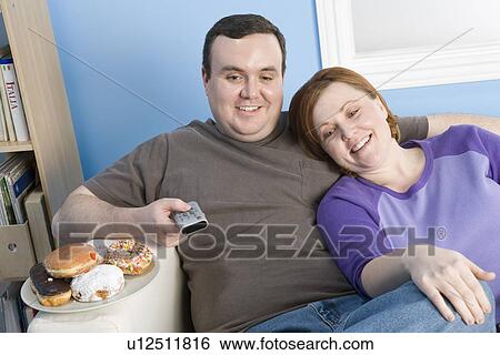 Overweight couple watching television on sofa View Large Photo Image Stock Photograph - Overweight couple watching television on sofa. Fotosearch