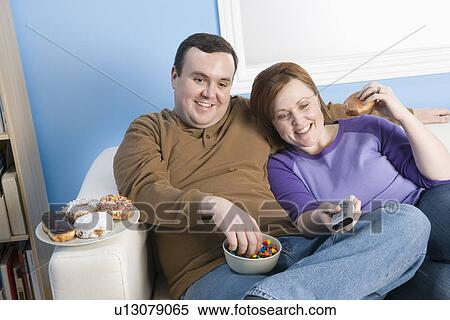 Overweight couple watching television on sofa View Large Photo Image Stock Photography - Overweight couple watching television on sofa. Fotosearch