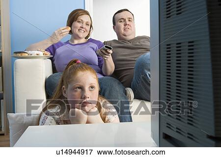 Stock Photo - Overweight family watching television on sofa. Fotosearch