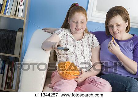 Stock Photo - Overweight girl and mother watching television on sofa. Fotosearch