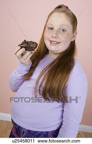Stock Image - Overweight girl holding brownie, portrait. Fotosearch