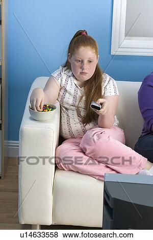 Stock Photo - Overweight girl watching television on sofa. Fotosearch