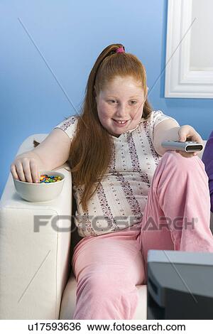Stock Photograph - Overweight girl watching television on sofa. Fotosearch