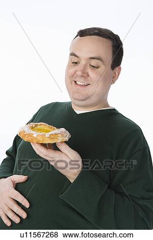 Stock Photo - Overweight mid-adult man holding pastry. Fotosearch