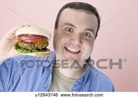 Stock Photograph - Overweight mid-adult man holding hamburger. Fotosearch
