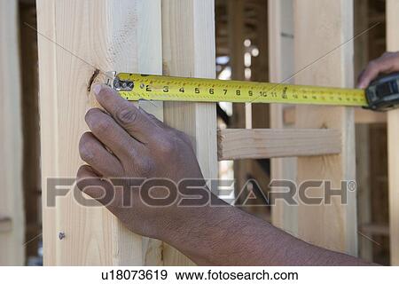 Stock Photo - Person measuring half constructed wall with tape measure. Fotosearch