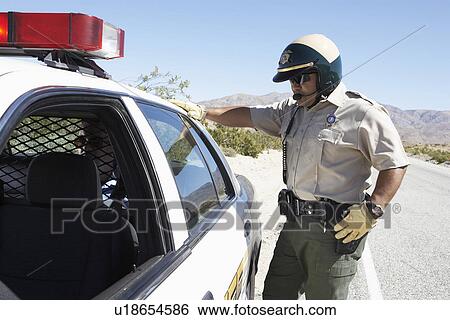 Police officer standing by police car on desert highway View Large Photo Image Stock Photograph - Police officer standing by police car on desert highway. Fotosearch