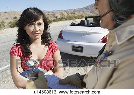 Stock Image - Police officer ticketing young woman driver on desert highway. Fotosearch