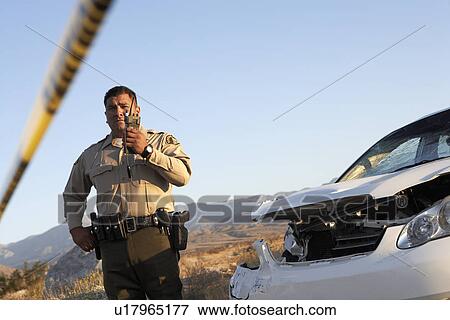 Police officer using walkie-talkie next to wrecked car View Large Photo Image Stock Photo - Police officer using walkie-talkie next to wrecked car. Fotosearch