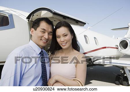 Portrait of mid-adult Asian business couple standing in front of private airplane. View Large Photo Image Picture - Portrait of mid-adult Asian business couple standing in front of private airplane.. Fotosearch