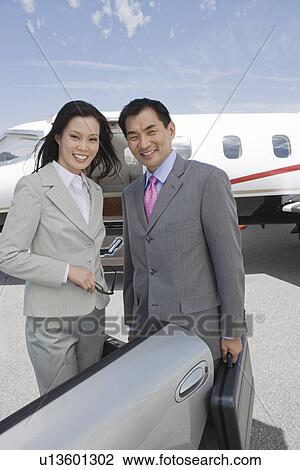 Stock Image - Portrait of mid-adult businesswoman and mid-adult businessman standing in front of private plane.. Fotosearch