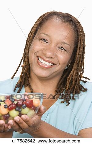 Stock Image - Portrait of Mid-adult overweight woman holding bowl wit fruit salad and smiling, close-up. Fotosearch