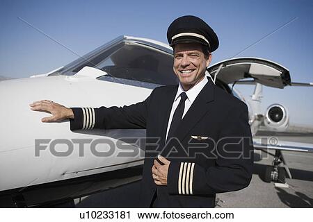 Stock Image - Portrait of pilot standing in front of airplane.. Fotosearch