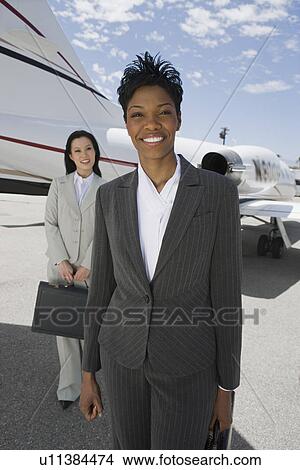 Picture - Portrait of two mid-adult businesswomen in front of private plane.. Fotosearch