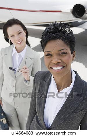 Stock Image - Portrait of two mid-adult businesswomen in front of private plane, elevated view.. Fotosearch