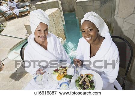 Stock Photo - Portrait of women in bathrobes eating by pool. Fotosearch
