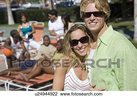 Stock Image - Portrait of Young Couple in Sunglasses, Others in Background. Fotosearch
