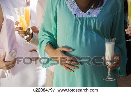 Stock Photo - Pregnant Woman with Glass of Milk at a Baby Shower, Mid Section. Fotosearch