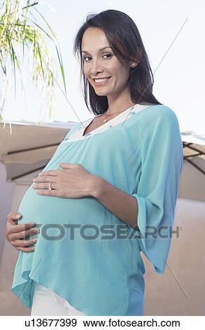 Stock Photo - Pregnant Woman with hands on stomach, outside. Fotosearch