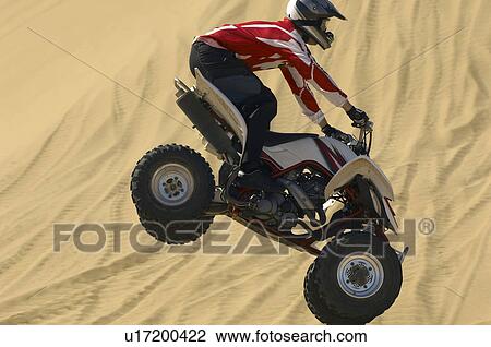 Quad bike rider in mid-air over sand, close-up View Large Photo Image Stock Image - Quad bike rider in mid-air over sand, close-up. Fotosearch