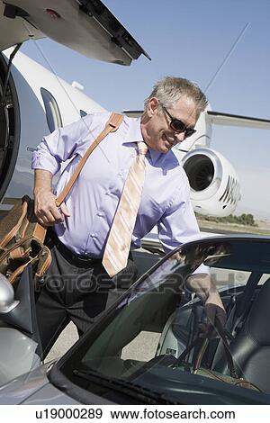 Stock Photo - Senior businessman getting of airplane and getting in car.. Fotosearch