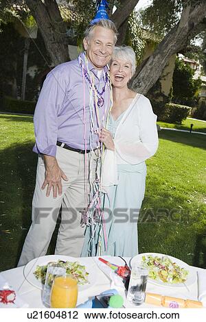 Stock Image - Senior couple embracing and smiling while birthday party in garden. Fotosearch