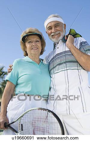 Stock Image - Senior couple holding tennis equipment, portrait. Fotosearch