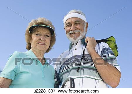 Stock Photo - Senior couple holding tennis equipment, portrait. Fotosearch