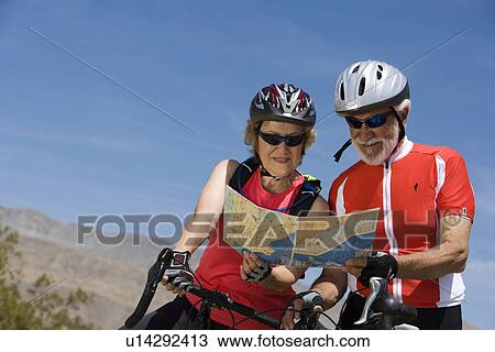 Stock Image - Senior couple with bikes reading map. Fotosearch
