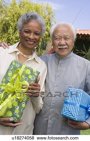 Stock Photo - Senior man and woman holding birthday presents, smiling. Fotosearch
