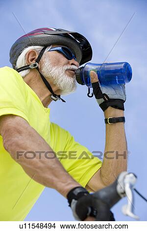 Picture - Senior man cycling and drinking water. Fotosearch