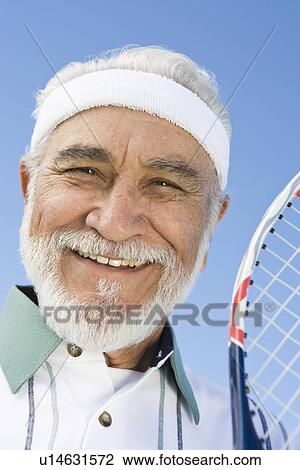Stock Image - Senior man holding tennis racket, portrait. Fotosearch