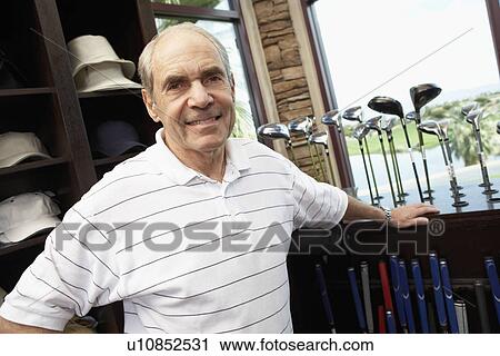 Stock Image - Senior man in golf shop, standing near display case of golf clubs. Fotosearch